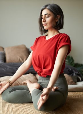 Indoor shot of fashionable gray haired young woman yogi practicing meditation in her bedroom, sitting in lotus pose, closing eyes and making mudra gesture. Yoga, health, energy and harmony